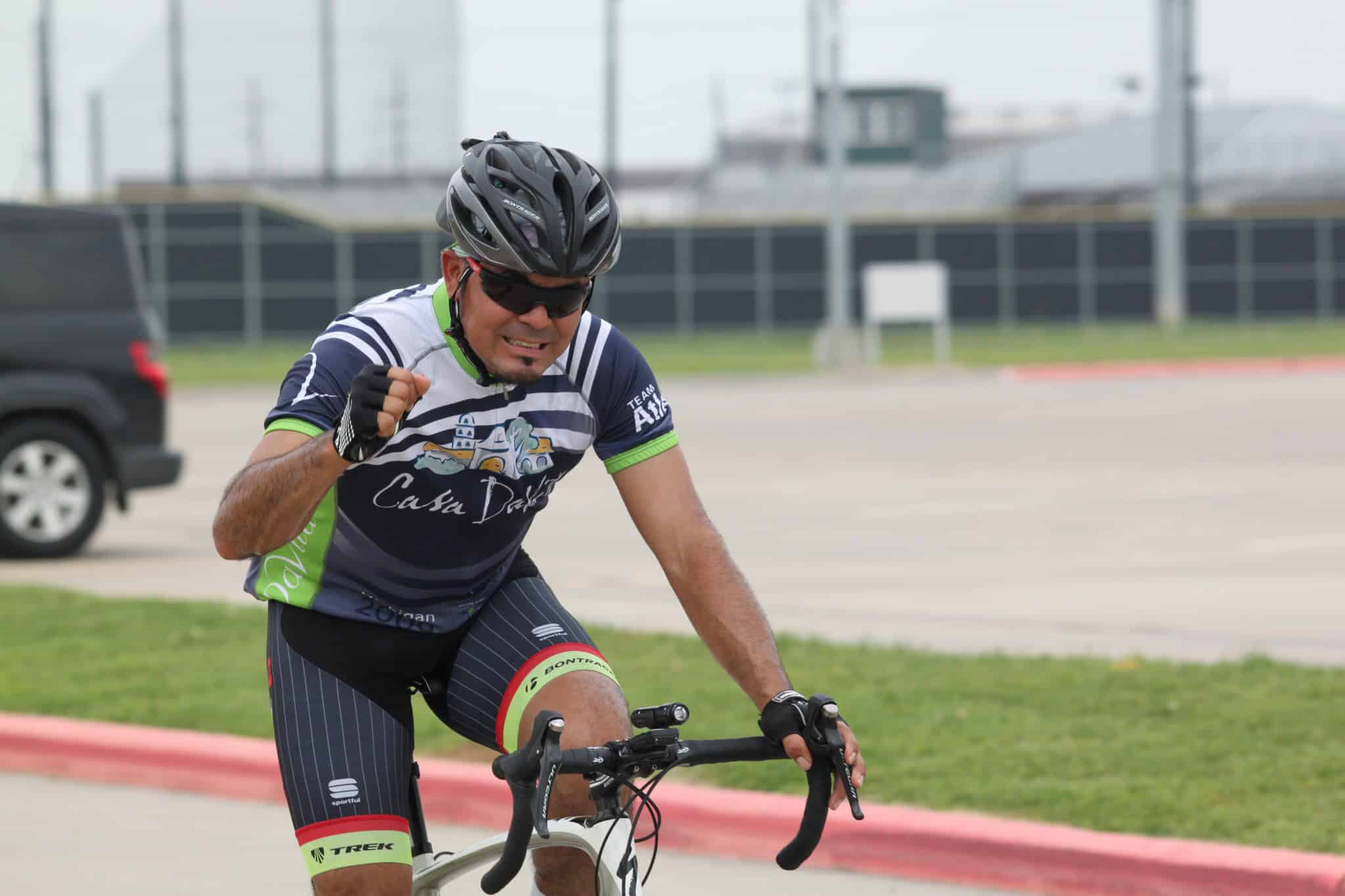 Vibrant cyclist wearing a blue and green custom jersey, riding on a paved path with a determined expression.