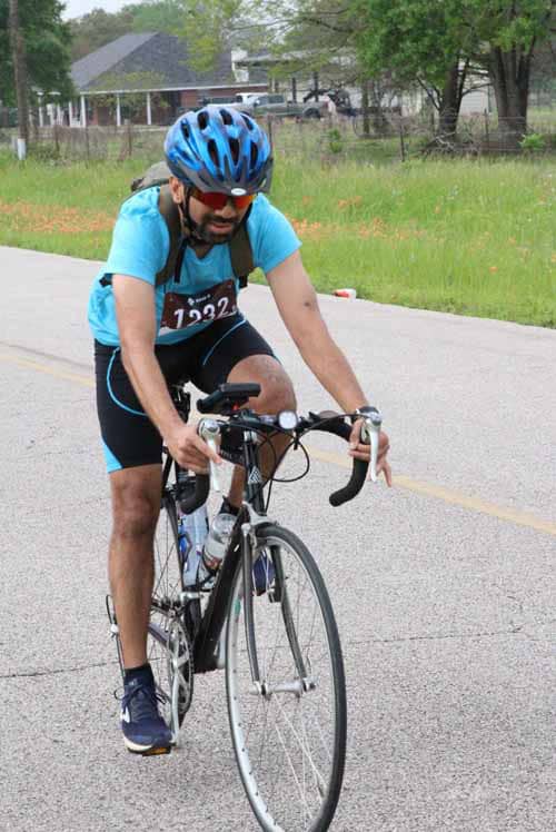 Man cycling during Bluebonnet Express race, wearing helmet and athletic gear, on a scenic road.