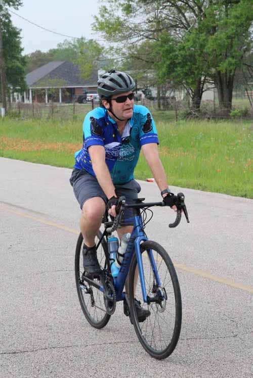 Man cycling on a road in a blue sports jersey and helmet during daytime.