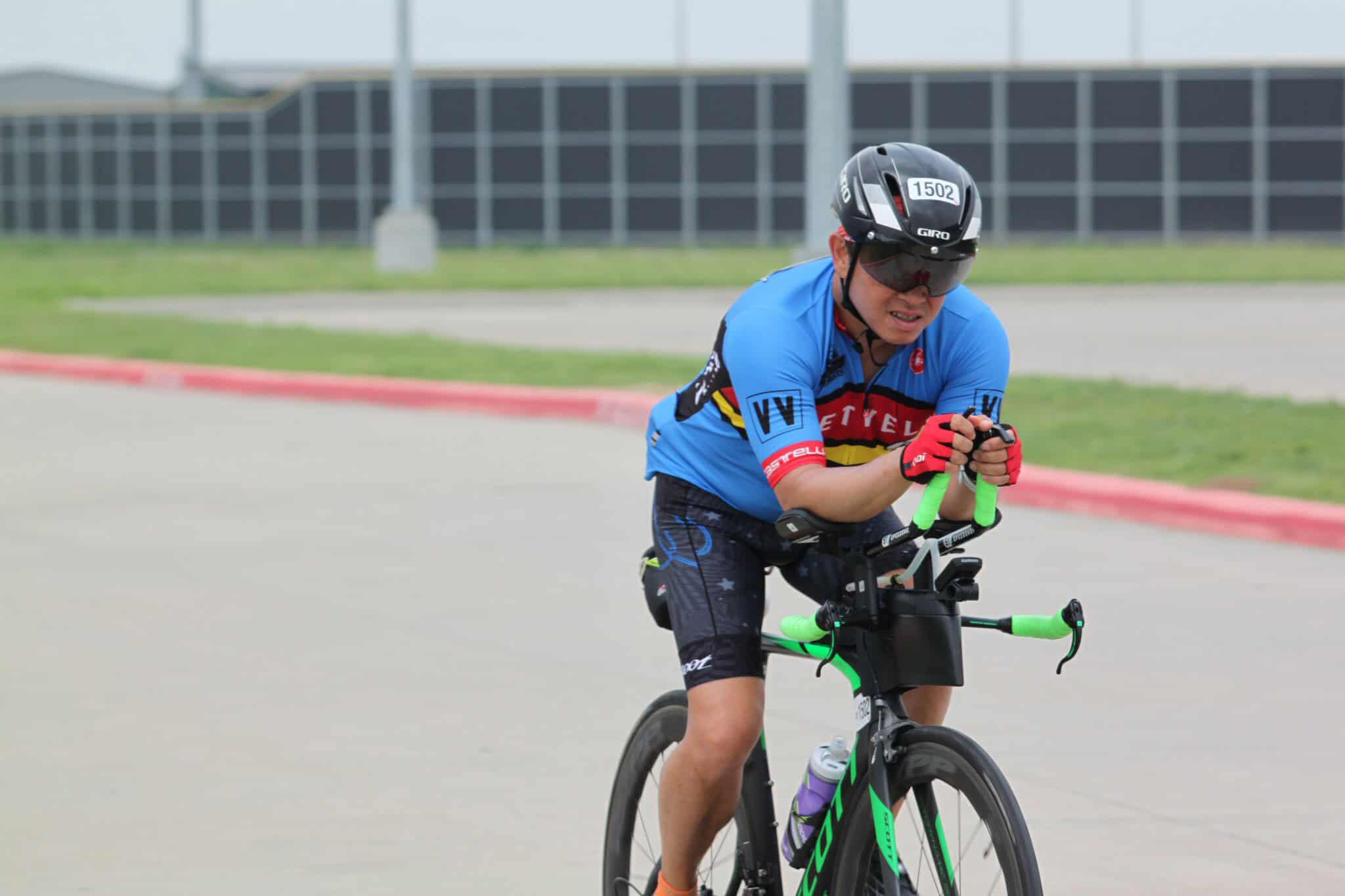 Velo cyclist racing outdoors, Bluebonnet Express branded gear, competitive cycling event, cycling race talent, adrenaline, focus, perseverance, leader, cycling sport.