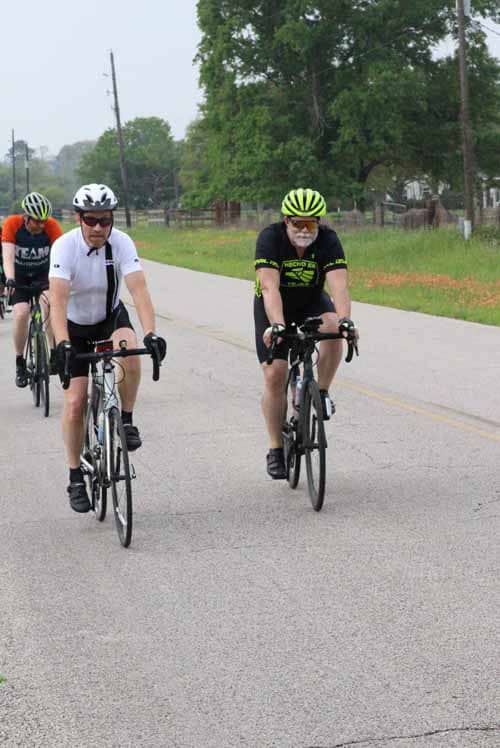 Bike riders enjoying a scenic ride on a country road with lush green trees in the background.