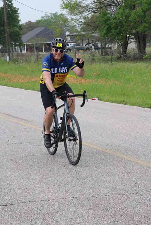 Bright cyclist wearing colorful jersey and helmet riding on rural road, promoting Bluebonnet Express bike event.