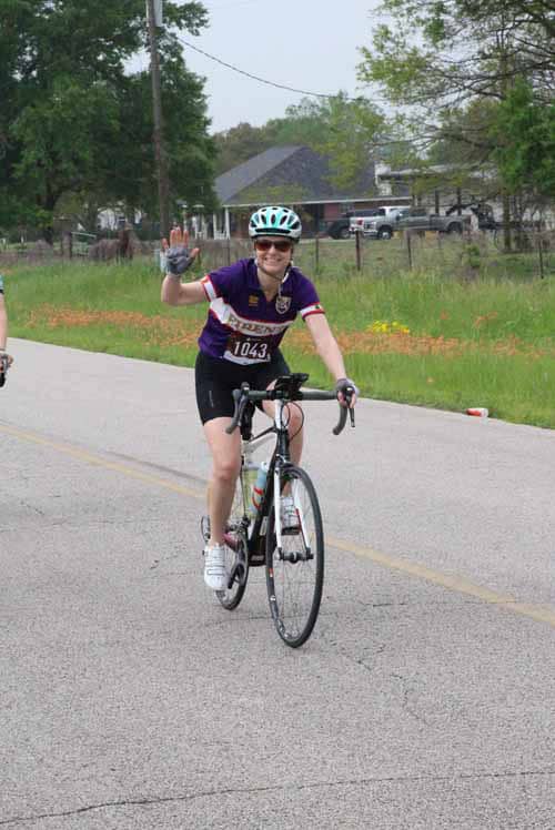 Smiling cyclist waving during Bluebonnet Express bike race on scenic rural road.
