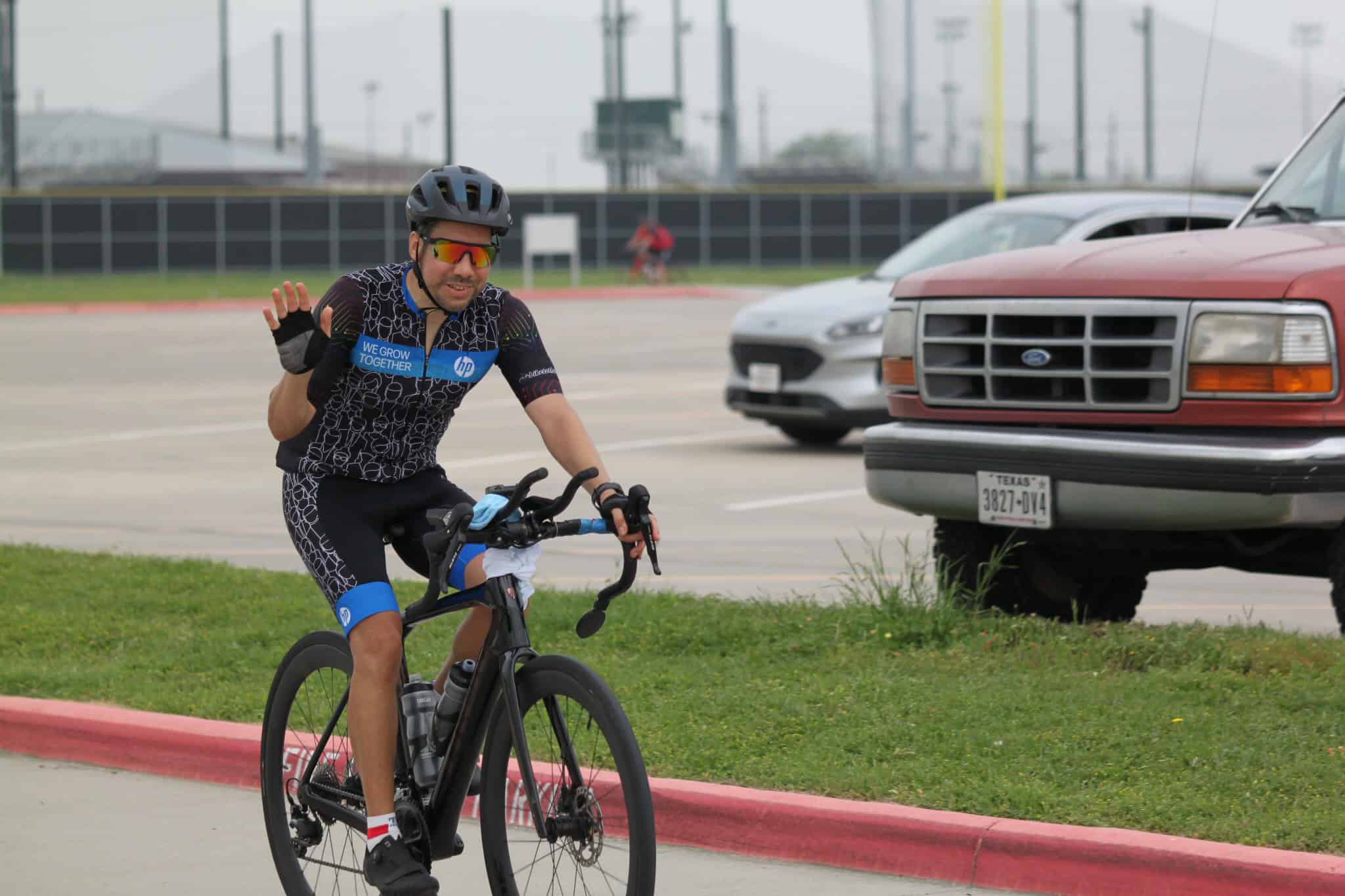 Bike rider waving during a cycling event in a parking lot, showcasing the adventure of Bluebonnet Express.