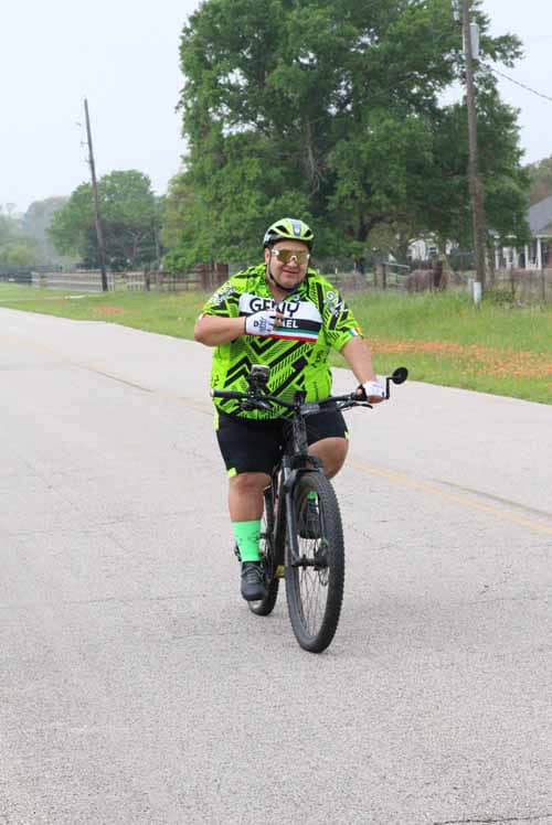 High-energy cyclist riding down rural road wearing bright green cycling jersey and helmet for Bluebonnet Express race.