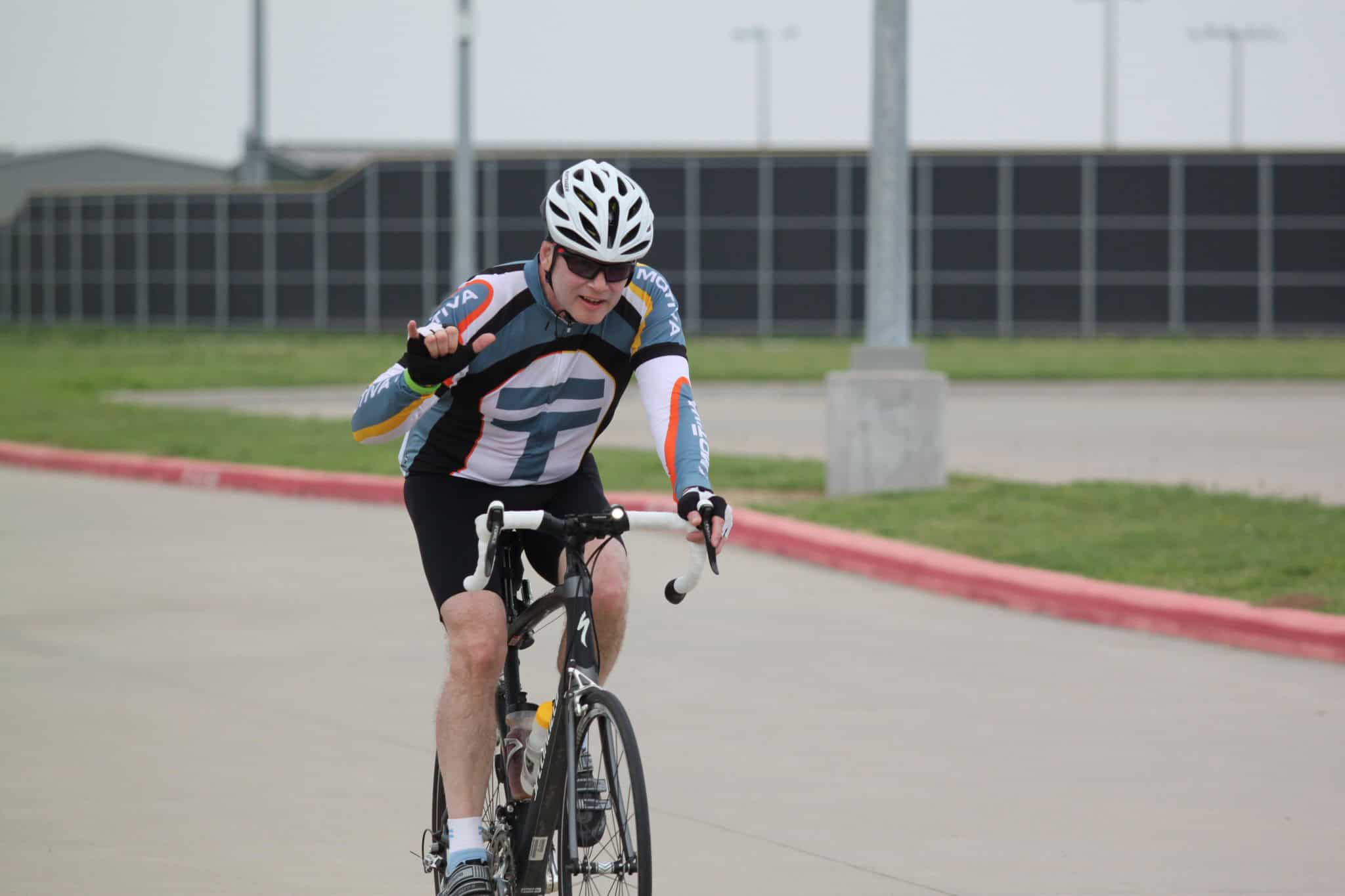 Bright male cyclist riding on the track in a Bluebonnet Express jersey, showcasing cycling endurance and sports performance.
