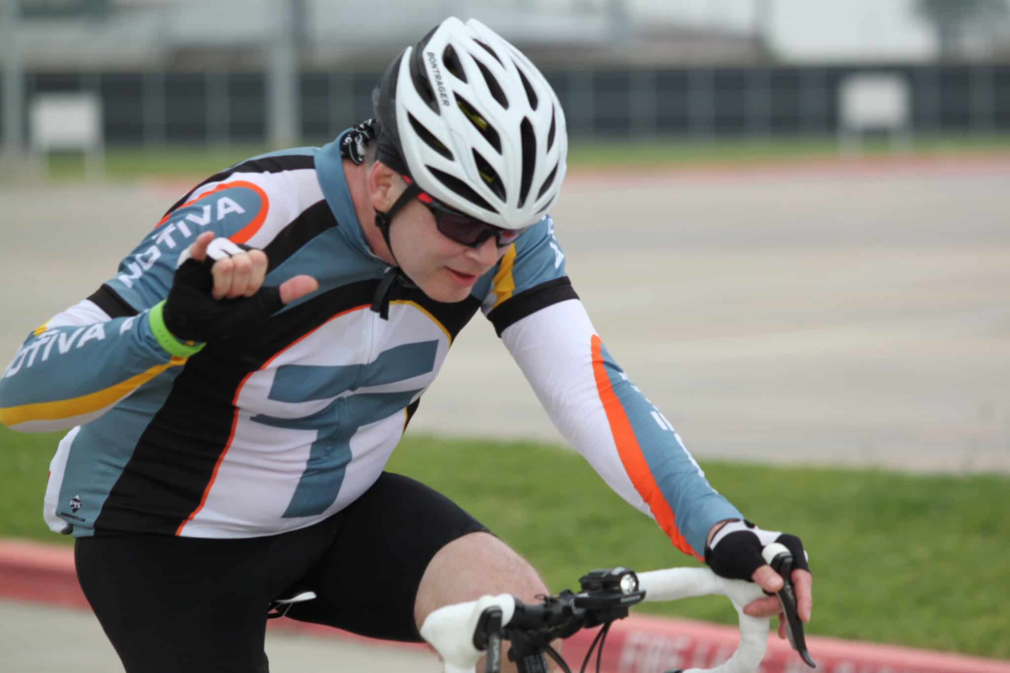 High-speed cyclist wearing Bluebonnet Express team gear at a race event, showcasing endurance and team spirit.