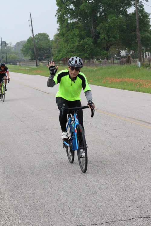 Rider in neon green cycling jersey waves on a peaceful countryside road during a bike ride.