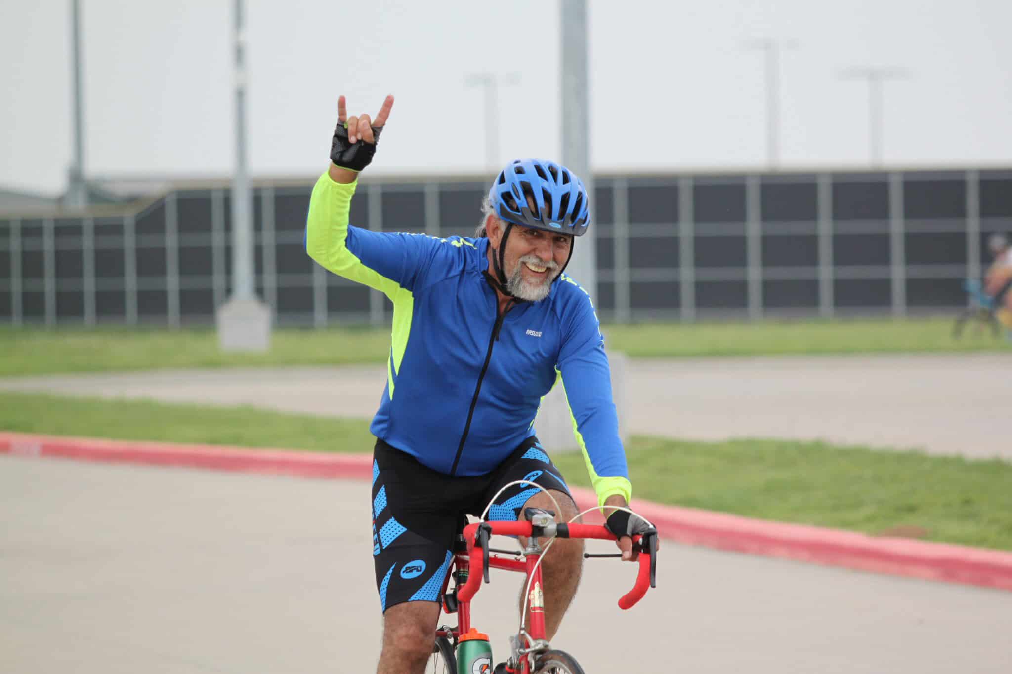 Bright blue and neon yellow cycling jersey with a man riding a red bike, making a victory sign.