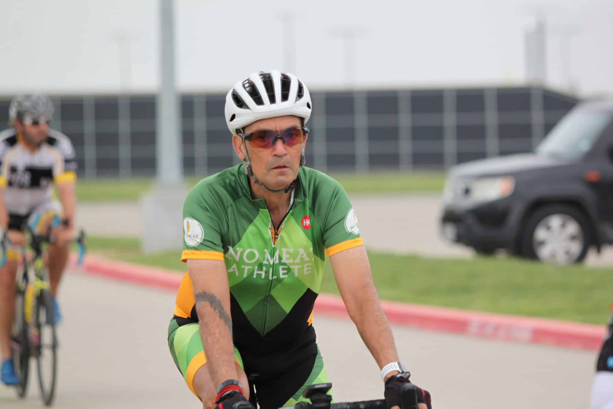 Bright green cyclist jersey with "No Meal Athlete" logo, riding outdoors during daytime.