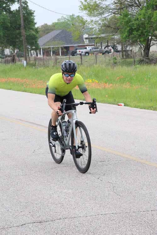 Bright male cyclist wearing yellow and black gear riding bicycle on rural road during daytime.