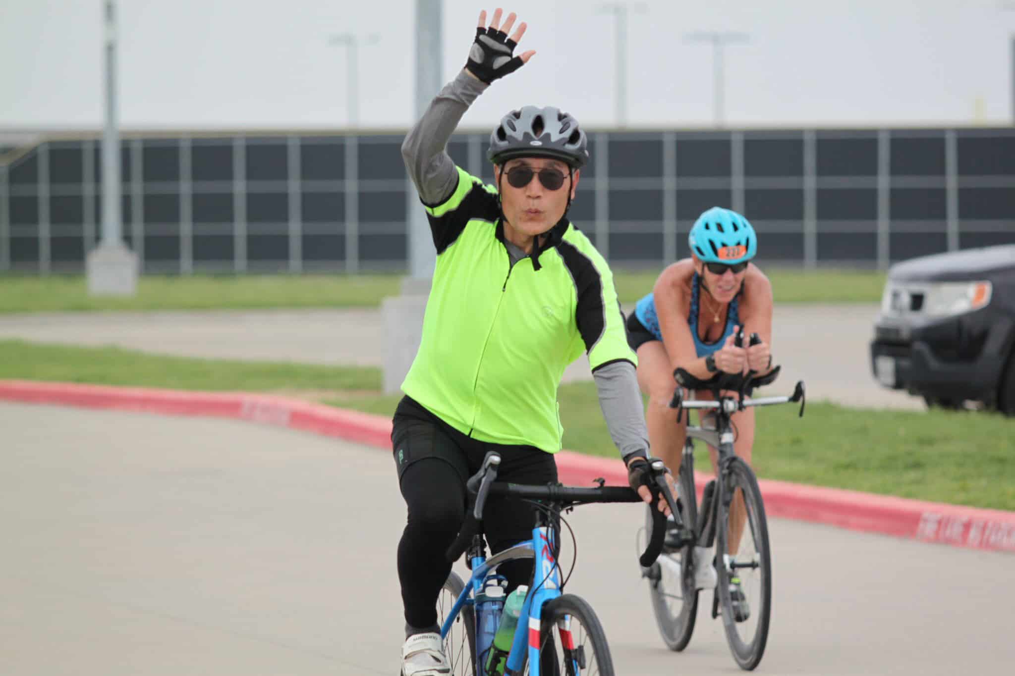 Bright neon cycling jersey on male cyclist waving at camera during Bluebonnet Express event.