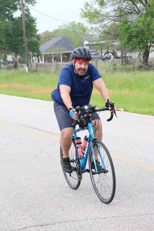 Man riding blue road bike on countryside road during daytime.