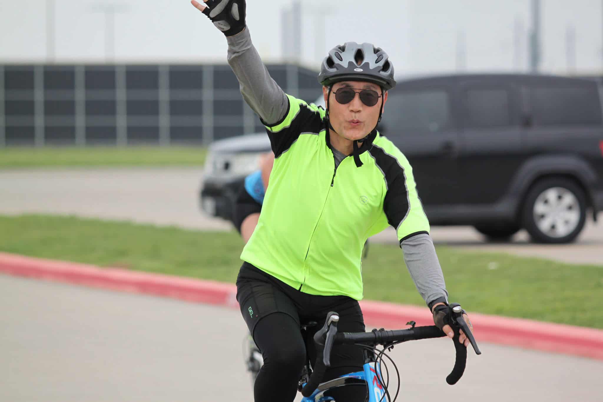Bright neon yellow cycling jersey, cyclist waving, on-road sport biking, Bluebonnet Express event, outdoor fitness.