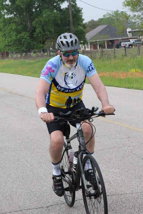 Man riding a bicycle on the road during daytime, wearing a helmet and sports gear for Bluebonnet Express event.
