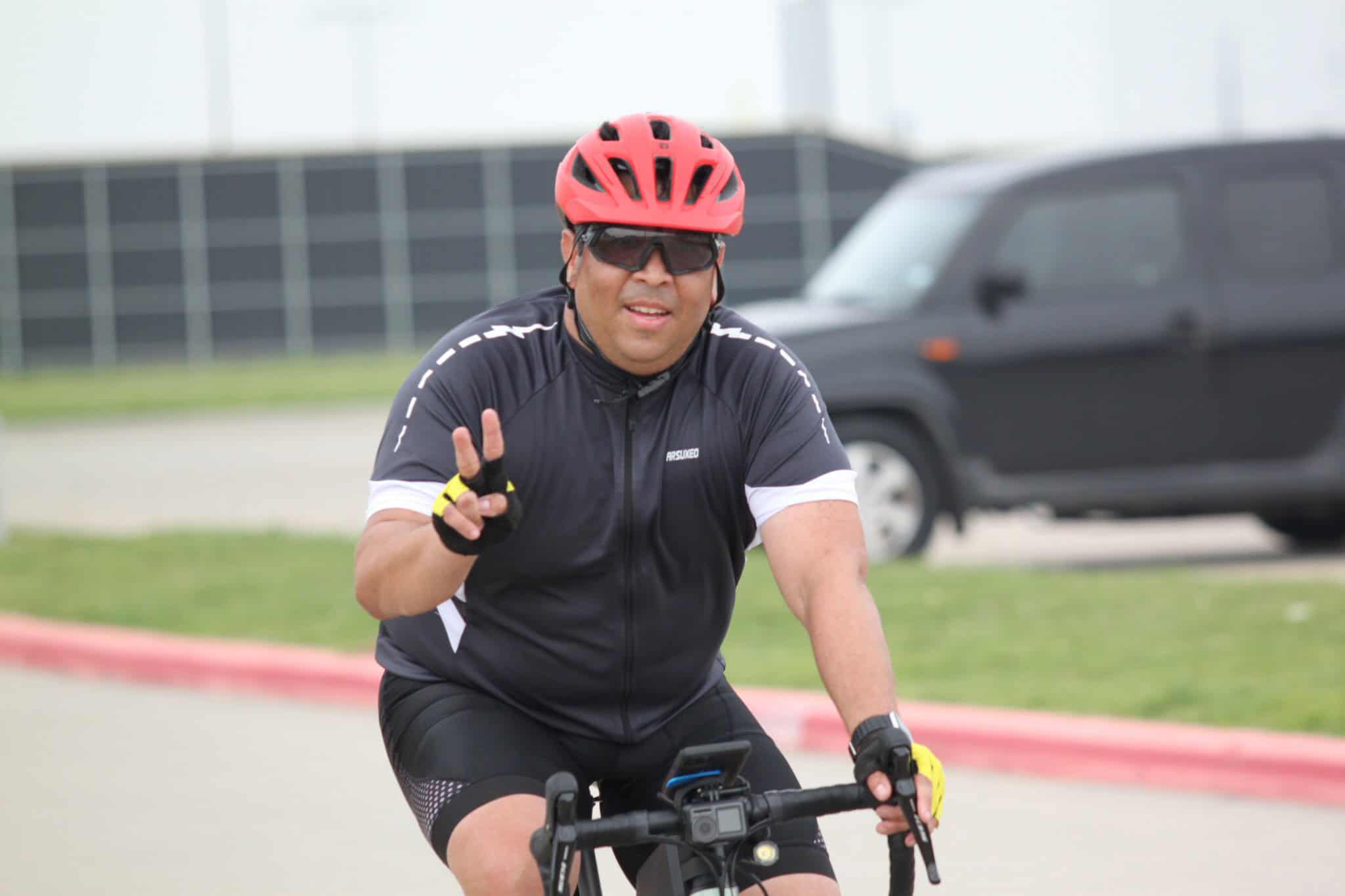 Active cyclist wearing red helmet and sunglasses, rural road scenery.