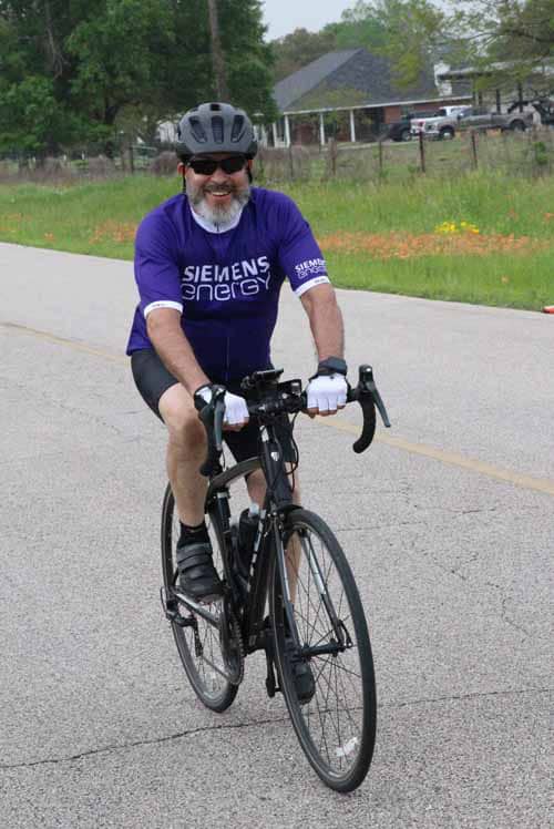 Bright smiling cyclist in Siemens Energy jersey riding a black bike on a scenic road.