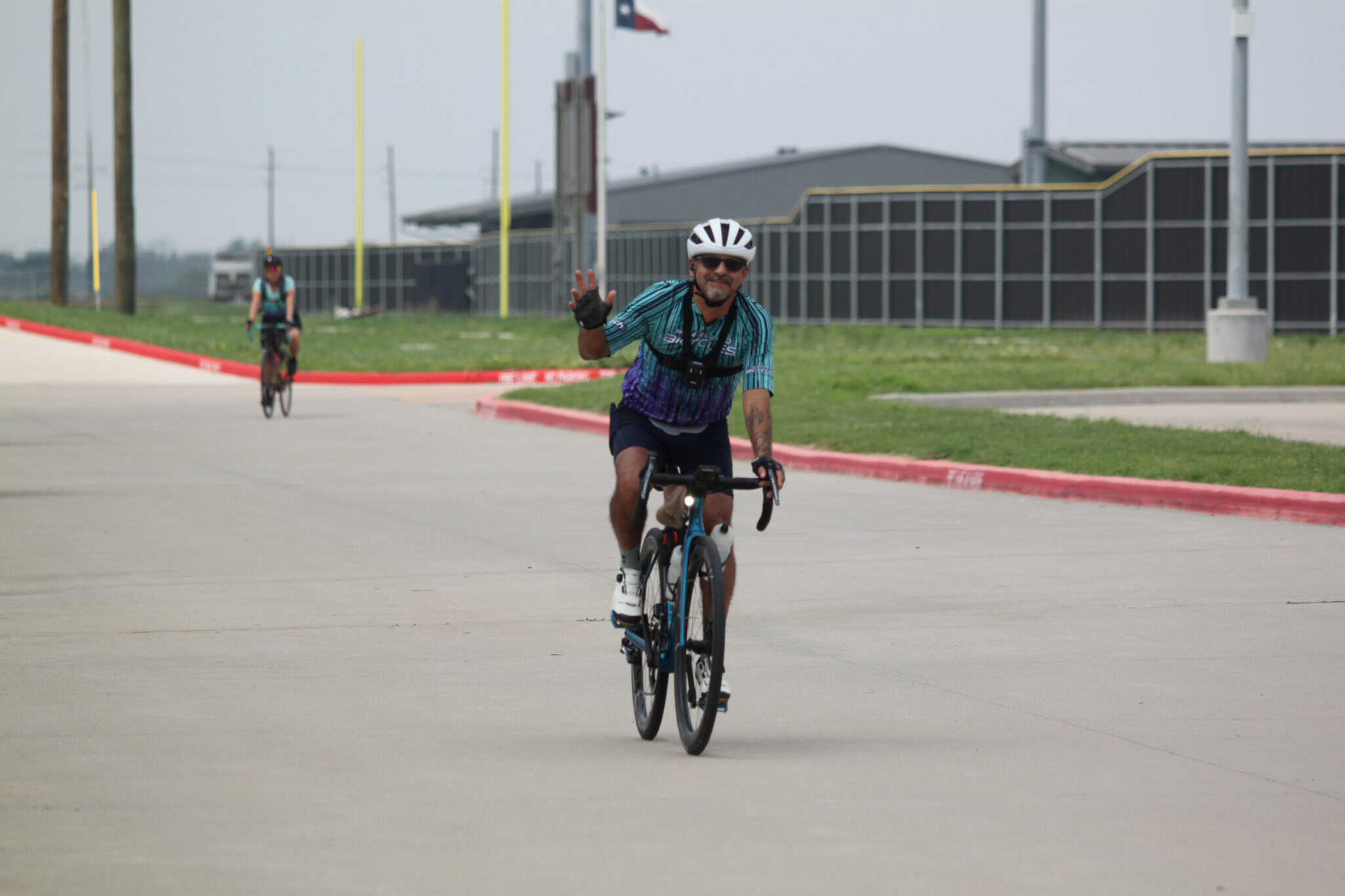 Enjoying a ride on the Bluebonnet Express bike trail in Texas. | Cycling adventure on Bluebonnet Express bike trail. | A cheerful cyclist waving while riding on the Bluebonnet Express bike trail in Texas, highlighting outdoor biking and community recreation.