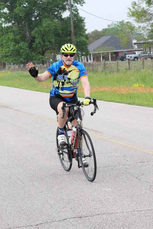 Cyclist waving on Bluebonnet Express bike tour in Texas, wearing colorful gear and helmet.