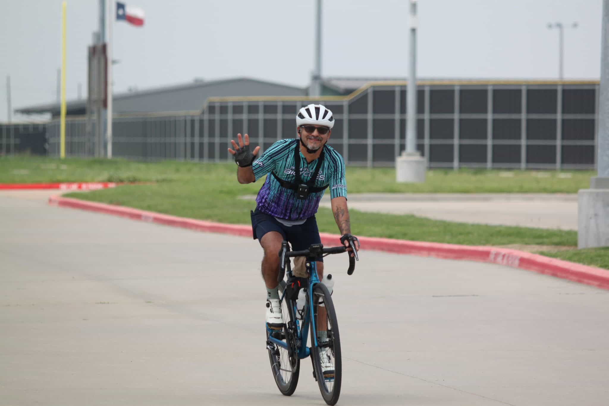 Energetic cyclist riding Bluebonnet Express bike, smiling and waving outdoors in Texas.