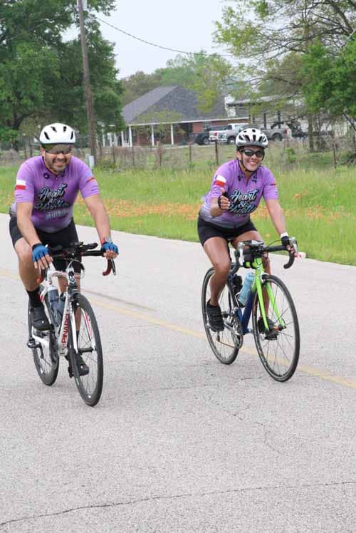 Active cyclists enjoying Bluebonnet Express ride on a rural road with green scenery and community background.