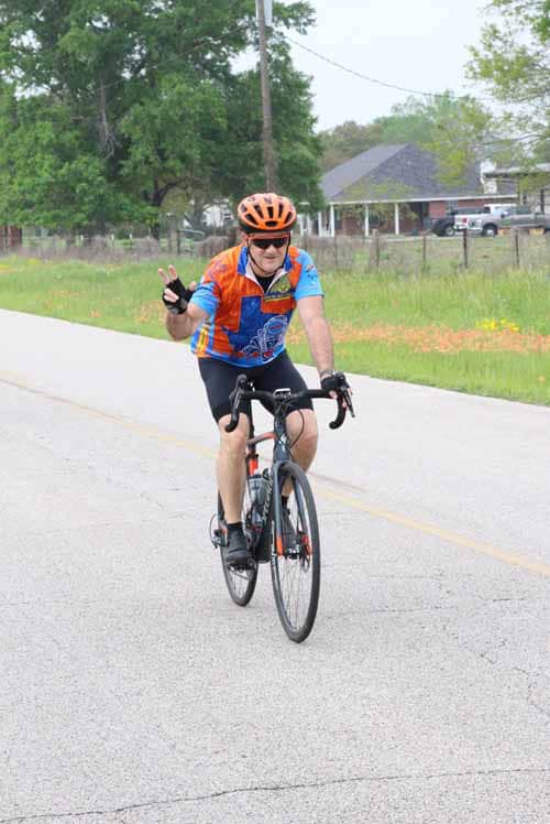 Bright-eyed cyclist riding on rural road during daytime, wearing colorful jerseys and safety helmets.