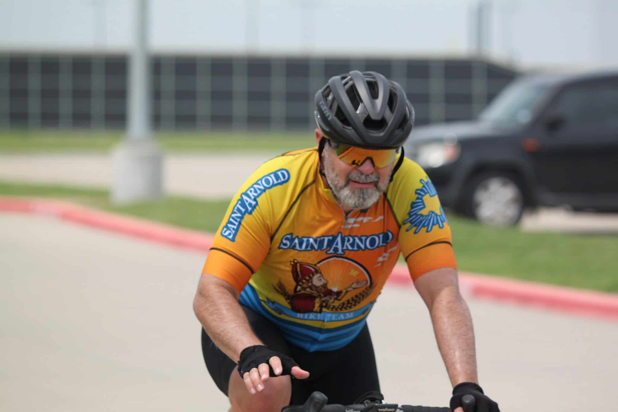 Bike rider wearing Saint Arnold cycling jersey and helmet on the road, enjoying a cycling race or ride.