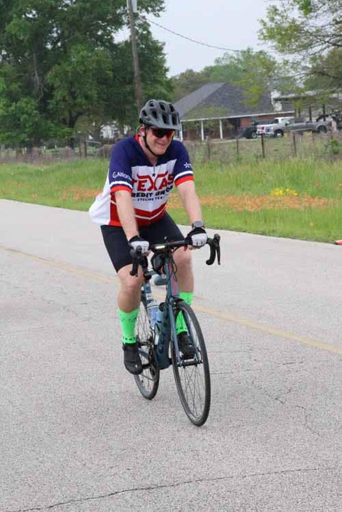 Cyclist riding on a rural road wearing a Texas-themed jersey and a helmet for safety.