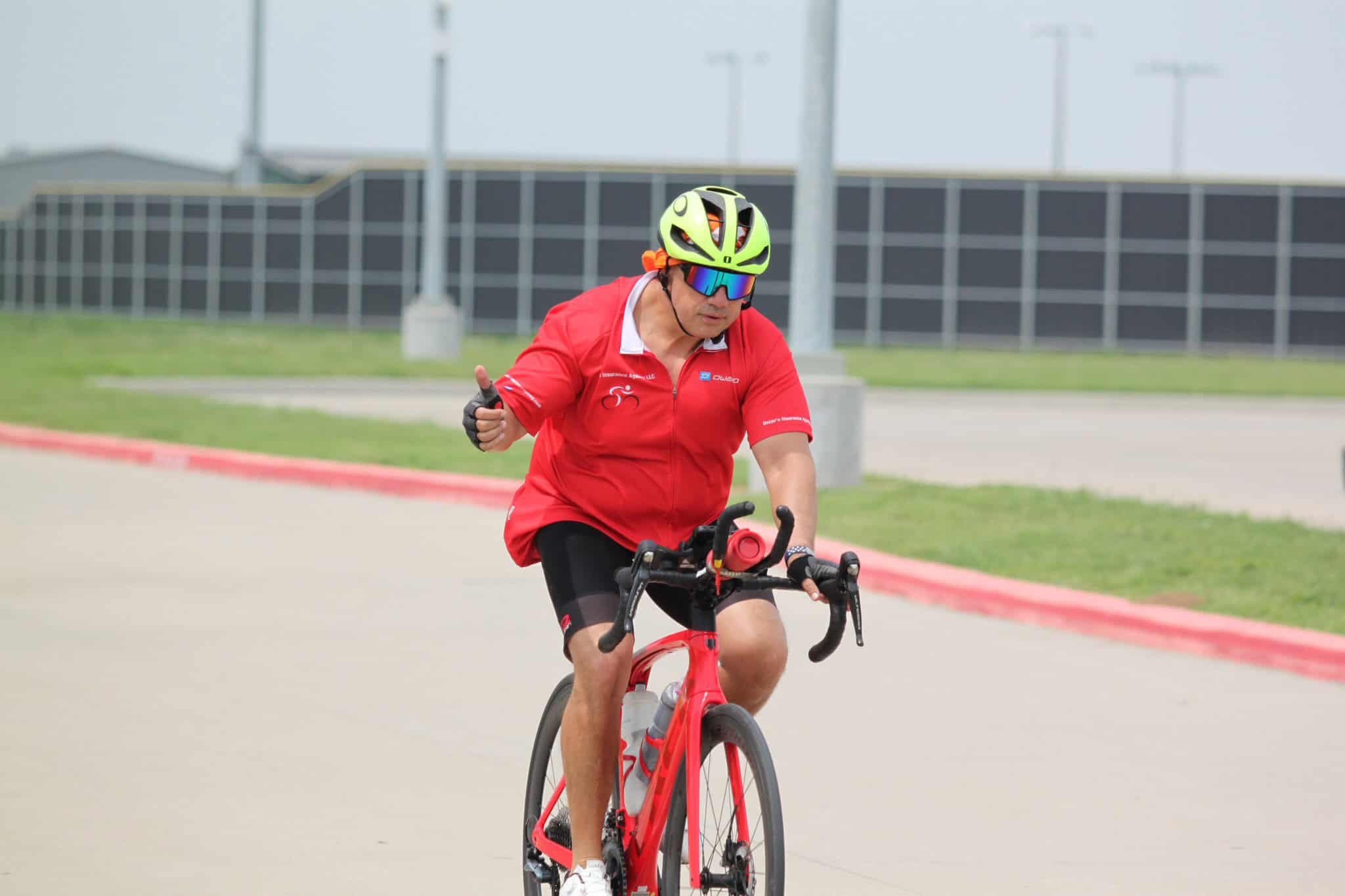 Bright cyclist in red gear giving thumbs up on a road bike during Bluebonnet Express event.