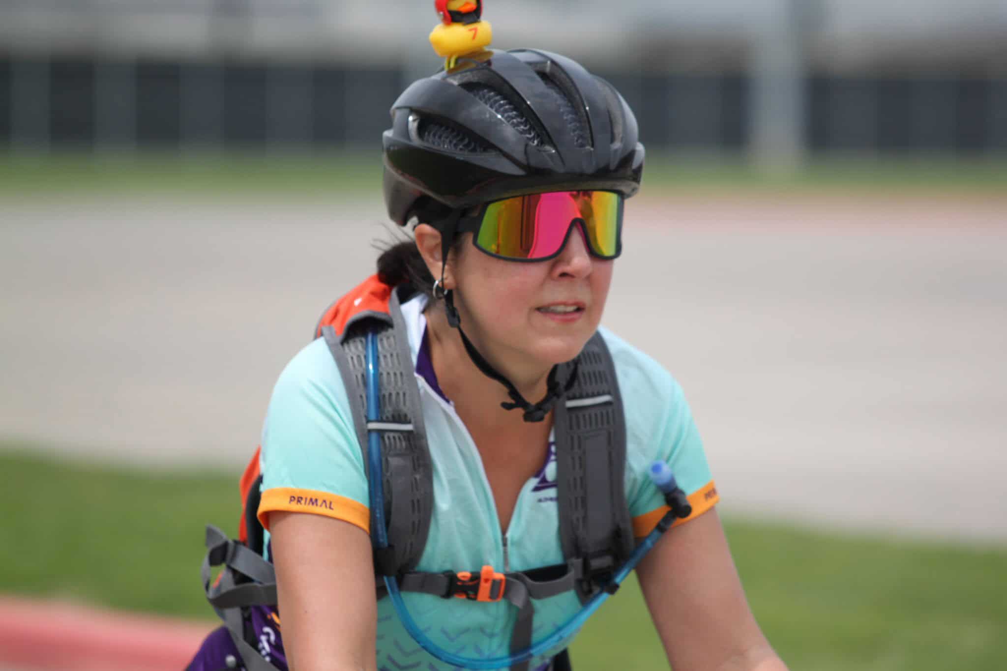 Vibrant cyclist with rainbow mirror sunglasses and black helmet, riding on a track for Bluebonnet Express.