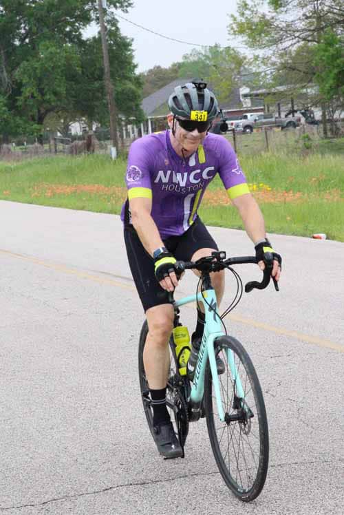 Bright purple cyclist jersey riding a road bike on a rural street during daytime.