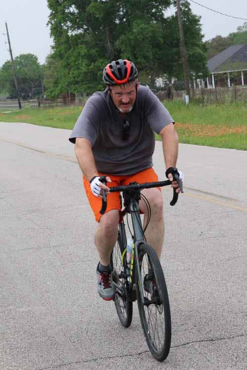 Bright male cyclist riding uphill on a black mountain bike during daytime.