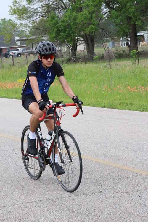 Teen boy riding a road bike wearing helmet on a suburban street during daytime.
