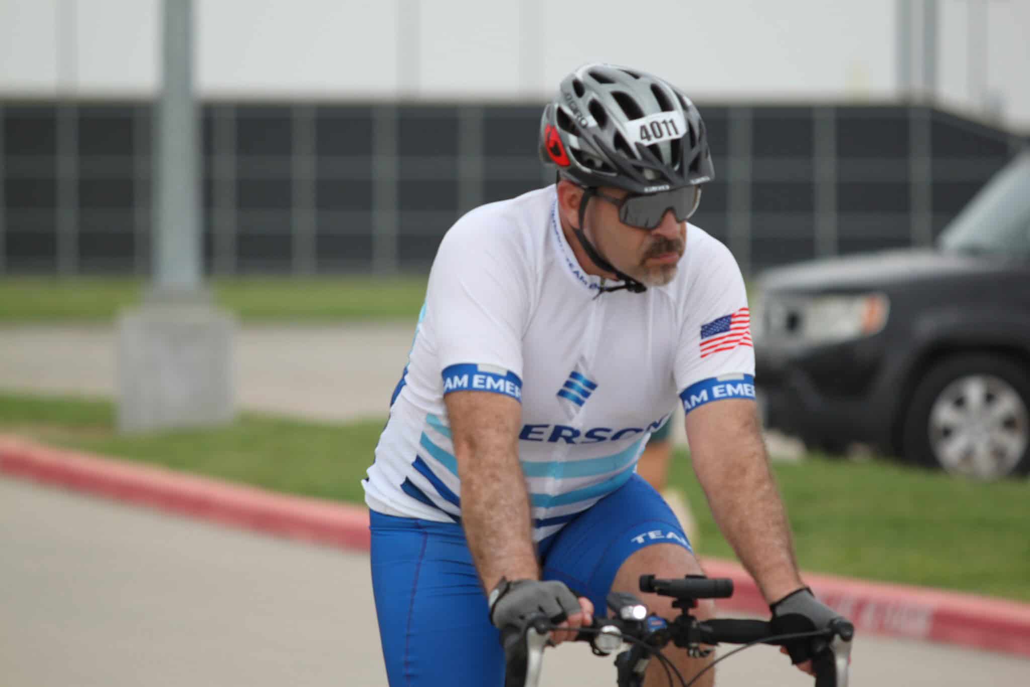 Avid cyclist wearing a white jersey with blue accents riding a bike outdoors.