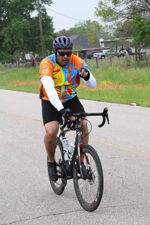 Helmeted cyclist riding on the road with colorful jersey, promoting Bluebonnet Express bike event.