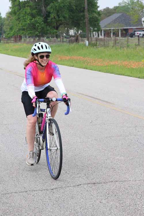 Enjoying a sunny day riding a bicycle on a scenic road with lush greenery and a charming neighborhood backdrop.