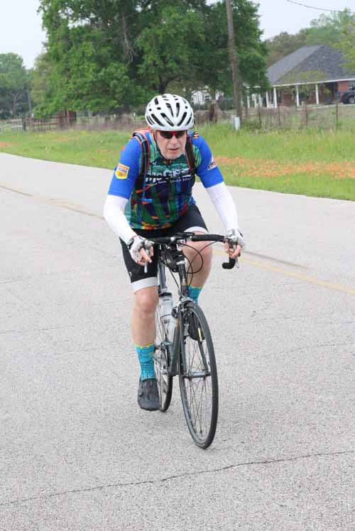 High-performance cyclist riding on scenic rural road during Bluebonnet Express event.