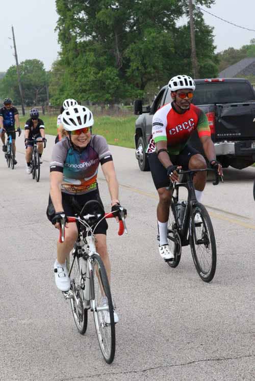 Smiling cyclists riding during Bluebonnet Express cycling event on a rural road, promoting outdoor fitness.