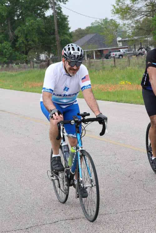 Bicyclist wearing white helmet and jersey riding on rural road during outdoor cycling event.