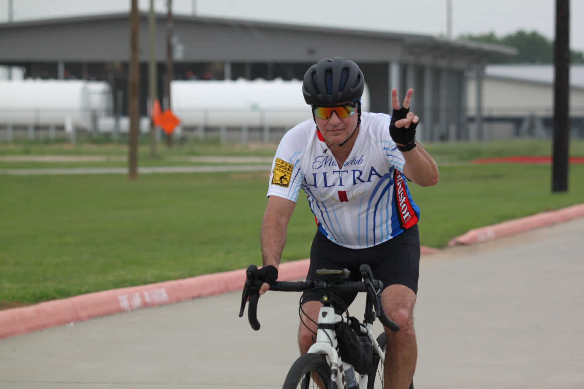 Bright male cyclist making peace sign during Bluebonnet Express event, enjoying bike ride.