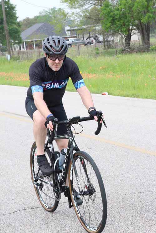 Cyclist riding on a rural road during daytime, promoting Bluebonnet Express biking event.