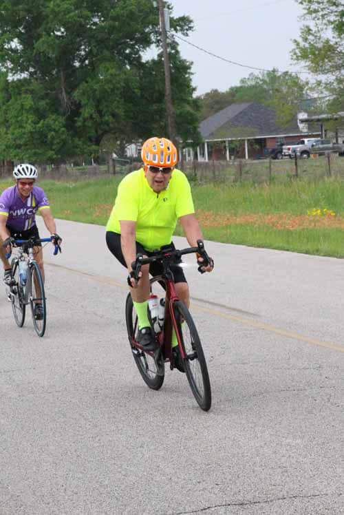 Bright yellow cyclist riding on scenic road during Bluebonnet Express event.