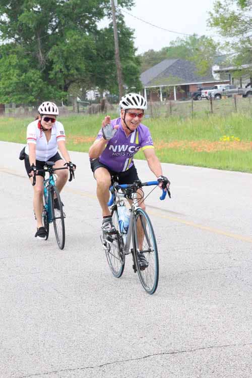 Joyful cyclists riding on a scenic road during a Bluebonnet Express event, promoting cycling and outdoor adventure.