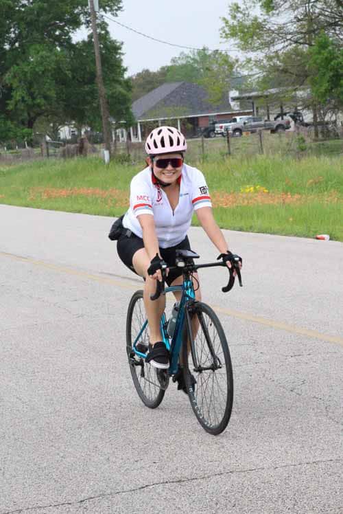 Bright female cyclist riding a road bike during daytime on a suburban street with greenery.