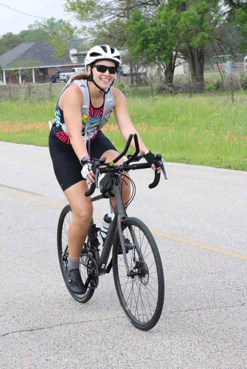 Bright smiling woman riding a black bicycle on a suburban street during daytime.