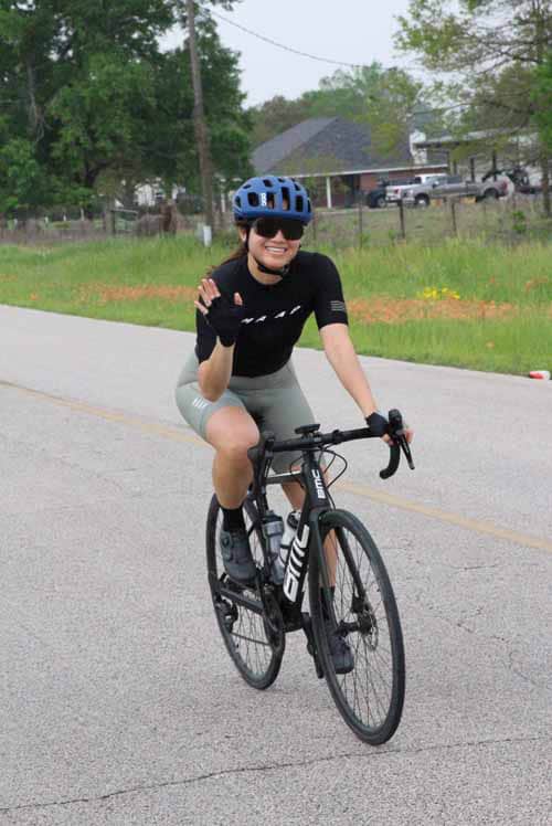 1. Woman riding Bluebonnet Express bike, wearing helmet and sunglasses, on a suburban road.
