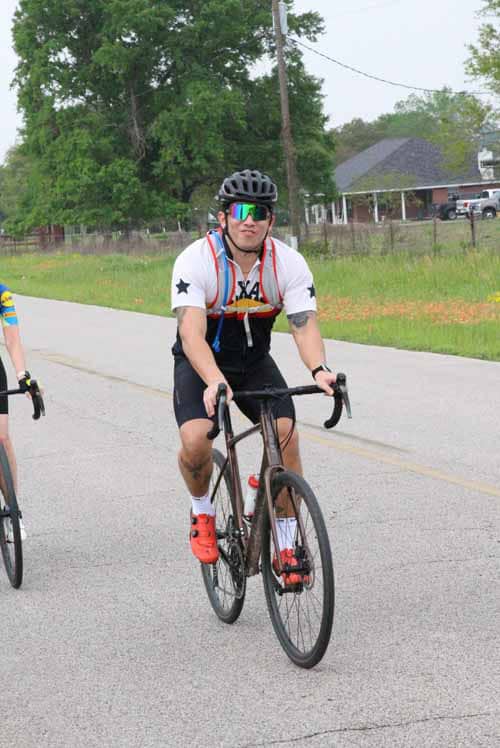 Vegan cyclist wearing helmet and sunglasses riding on a city street for Bluebonnet Express event.
