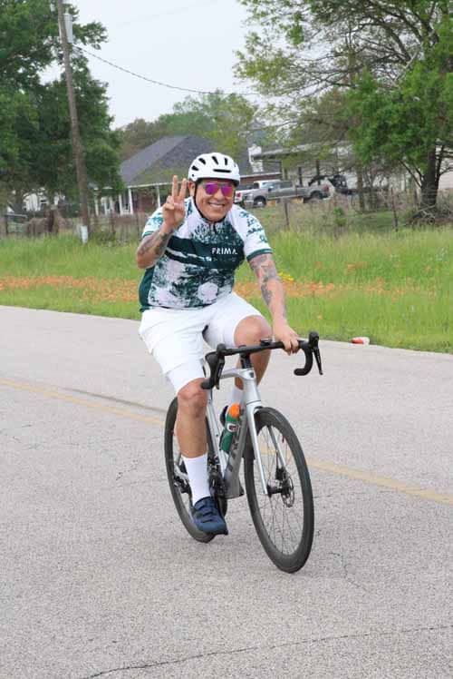 Bright cyclist in helmet making peace sign during Bluebonnet Express ride.