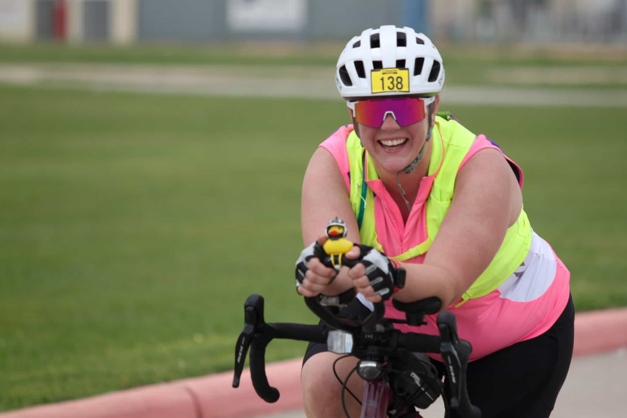 Bright smiling woman cycling, wearing helmet and sunglasses, enjoying Bluebonnet Express event.