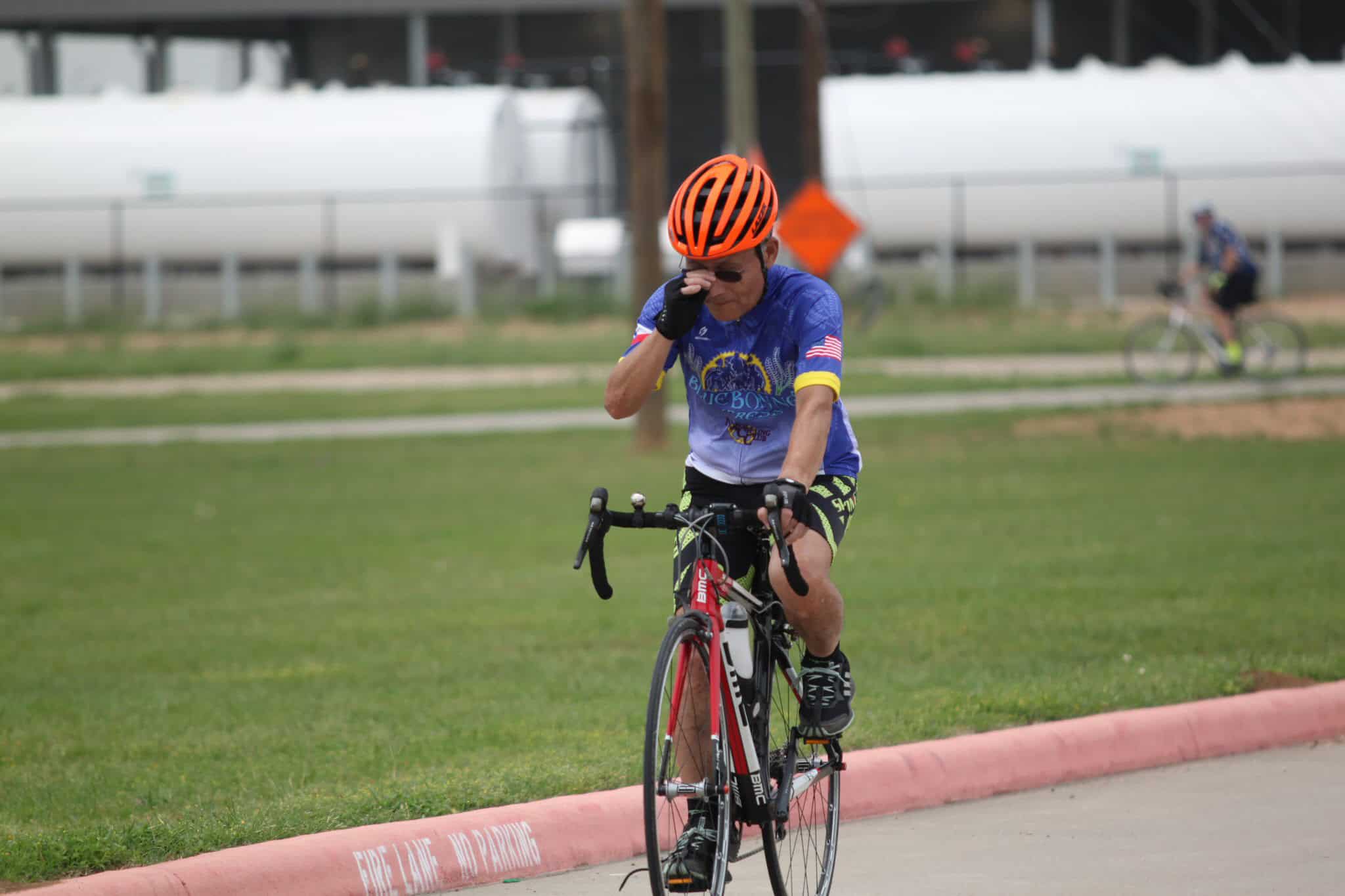 Rider wiping sweat during Bluebonnet Express bike race on a sunny day in Texas.